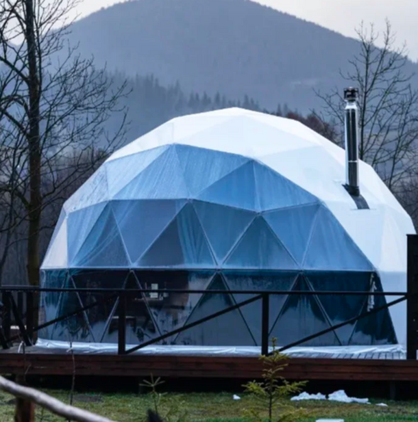 Geodesic dome structure in a natural setting with mountains in the background